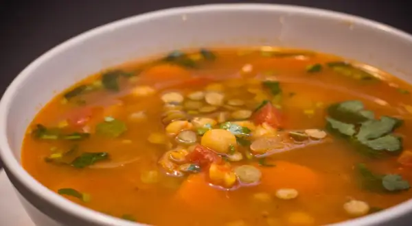 Aromaticzna zupa z ciecierzycy z kawałkami pomidorów, marchewki i świeżą kolendrą.