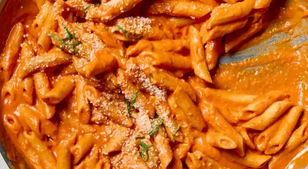 Penne alla vodka w kremowym, pomarańczowym sosie, posypane parmezanem i bazylią. Pyszne danie gotowe do podania.