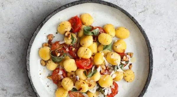 Pyszne gnocchi z sosem pomidorowym, listkami szałwii i orzechami na talerzu.