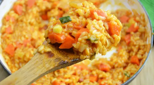 Kremowe risotto pomidorowe z kawałkami marchewki i cukinii, nabierane drewnianą łyżką.