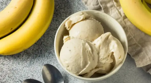 Pyszne lody bananowe w miseczce, obok świeże banany i łyżeczki. Idealne na upalne dni.