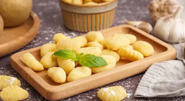 Pyszne, domowe gnocchi na drewnianej desce. Idealny przepis na obiad. W tle czosnek i ziemniaki.