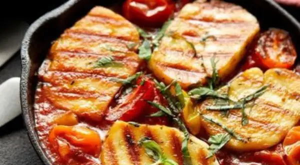 Pyszne halloumi z piekarnika w sosie pomidorowym z ziołami, podane w żeliwnej patelni.