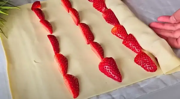 Słodkie truskawki w cieście francuskim układane w rzędach, gotowe do pieczenia.