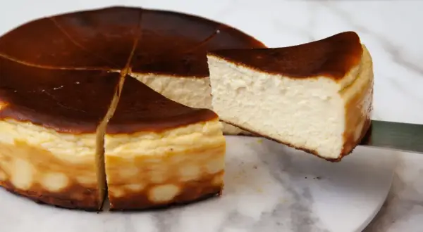 Kawałek pysznego, lekko przypieczonego basque cheesecake jest wyjmowany z całego ciasta.