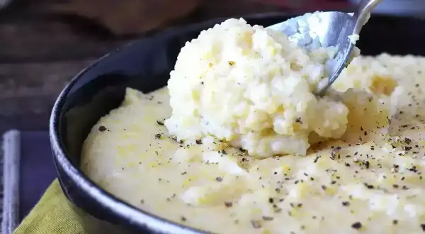 Kremowa polenta, idealna do prostego przepisu. Łyżka wydobywa porcję tej pysznej potrawy, posypanej pieprzem.