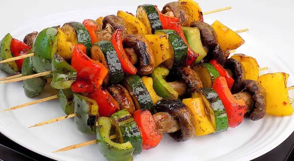 Kolorowe szaszłyki warzywne z papryką, cukinią i pieczarkami, grillowane do perfekcji, prezentują się apetycznie na białym talerzu.