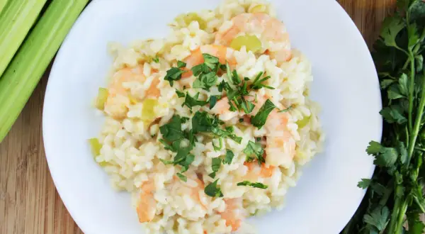 Kremowe risotto z krewetkami, posypane świeżą natką pietruszki, obok łodygi selera i oliwy.