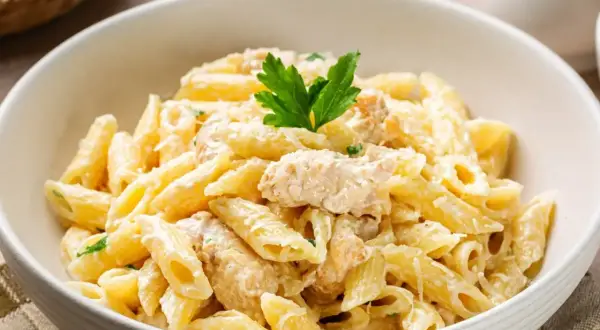 Pyszny makaron penne w kremowym sosie z kawałkami kurczaka, udekorowany natką pietruszki. Idealny na szybki obiad.