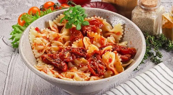 Pyszny makaron farfalle z aromatycznymi suszonymi pomidorami, udekorowany świeżą bazylią.
