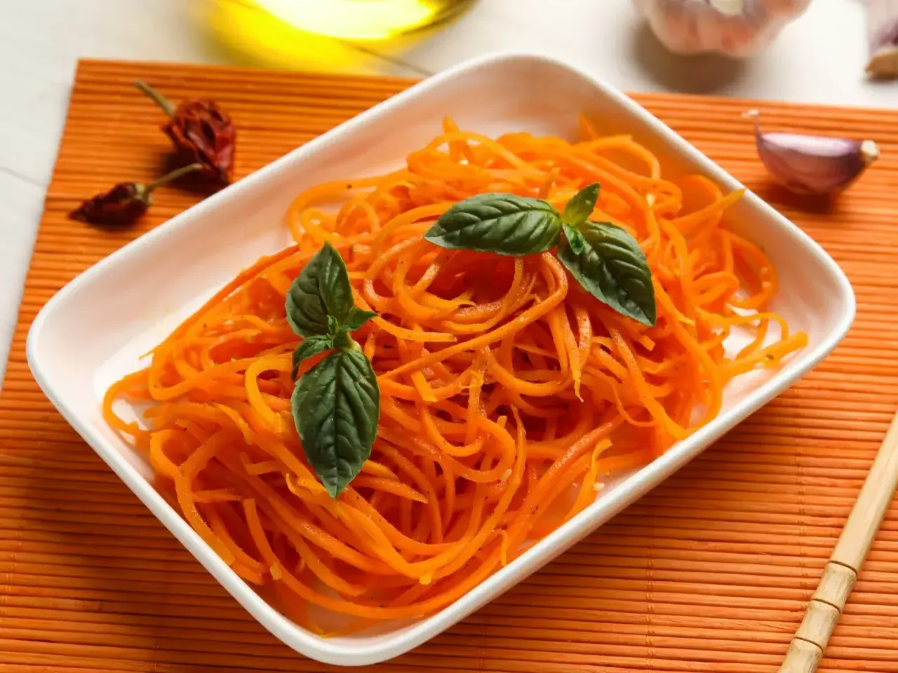Pyszna surówka z marchewki, udekorowana listkami bazylii, obok czosnku i papryczek chili.
