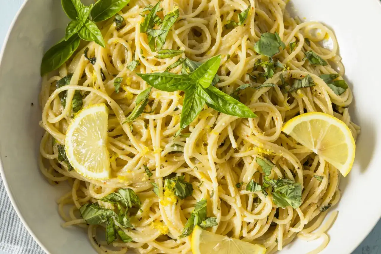 Pyszne spaghetti al limone z bazylią i plasterkami cytryny, posypane sk&oacute;rką cytrynową.