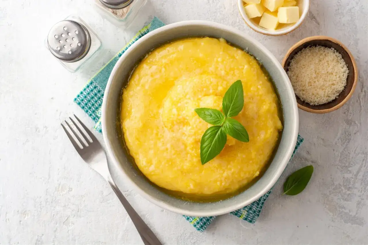 Pyszna polenta przepis na szybki obiad. Podana z parmezanem i masłem, udekorowana bazylią.