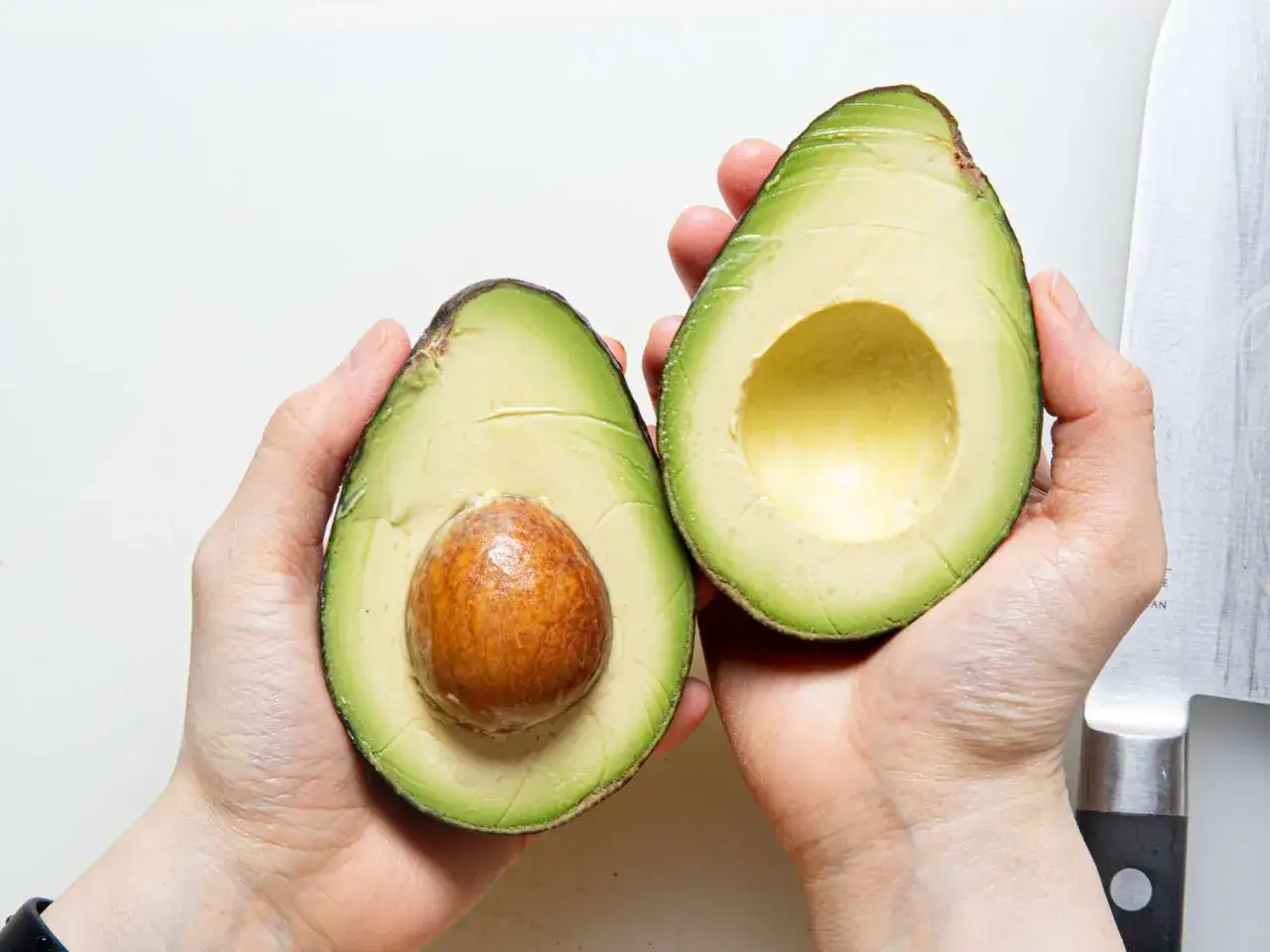 Dwie połówki awokado hass w dłoniach. Jedna z pestką, druga pusta, gotowa do przygotowania guacamole.