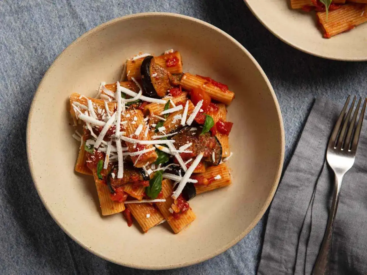 Pyszne rigatoni alla norma z bakłażanem, pomidorami i bazylią, posypane startym serem.