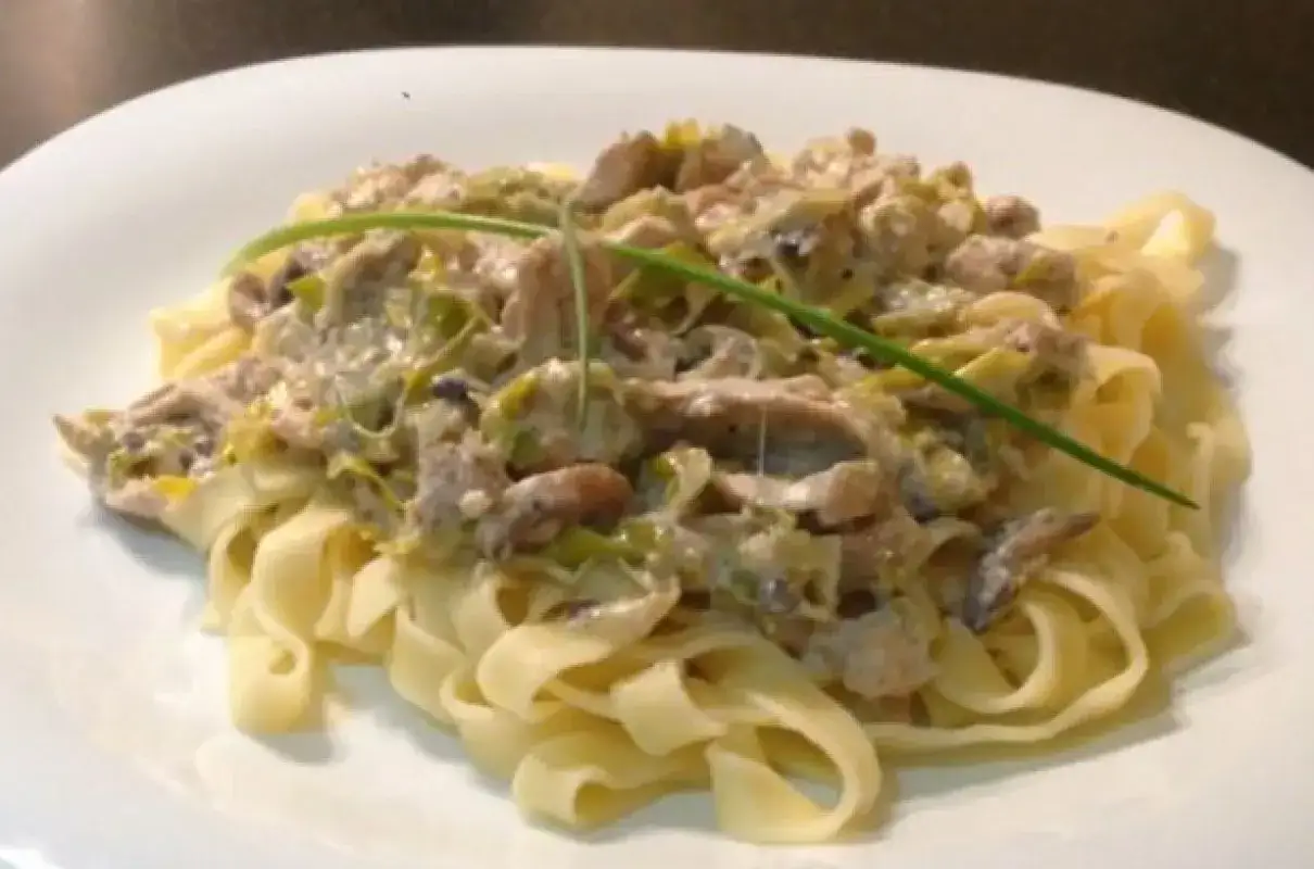 Pyszne makaron tagliatelle z kremowym sosem grzybowym i porem, udekorowane szczypiorkiem.