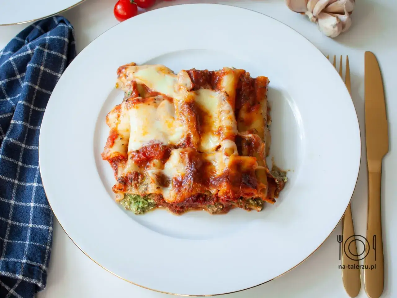 Pyszne cannelloni ze szpinakiem, zapieczone pod sosem pomidorowym i ciągnącym się serem, na białym talerzu.