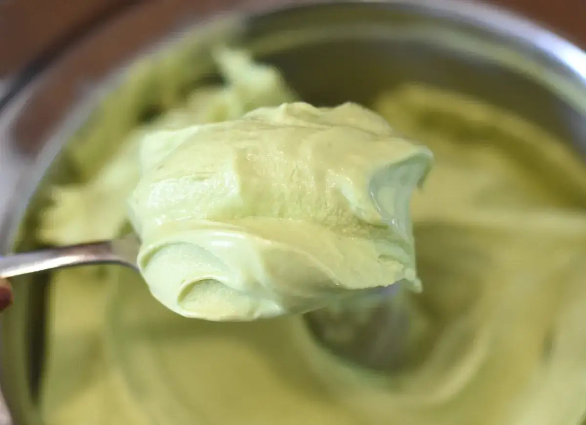 Łyżka zanurzona w kremowej, jasnozielonej masie pistacjowej, która wygląda jak pyszne lody.