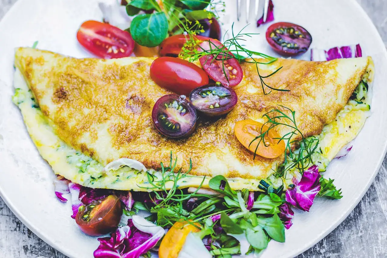 Złocisty omlet z cukinią, podany z kolorowymi pomidorkami i świeżą sałatką. Pyszne śniadanie.