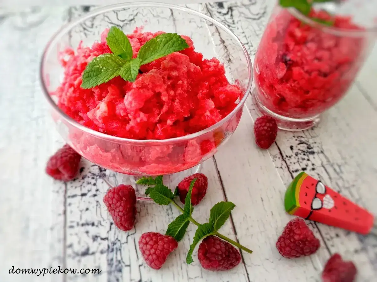 Malinowa granita przepis na orzeźwiający deser. W misce i szklance mrożony owocowy deser, ozdobiony listkami mięty i malinami.