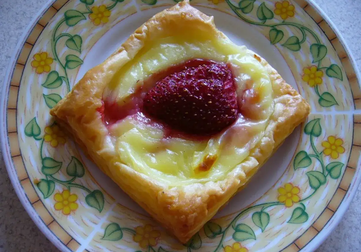 Słodkie ciasto francuskie z budyniem i truskawką na talerzu z kwiatowym wzorem.
