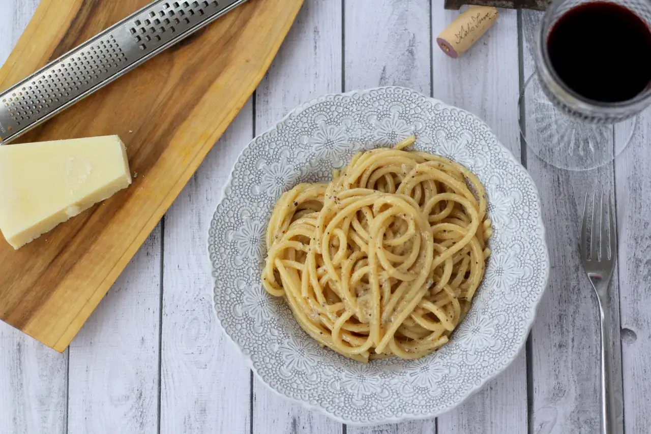 Pyszne cacio e pepe na talerzu, obok kawałek parmezanu i tarka. Idealny posiłek.