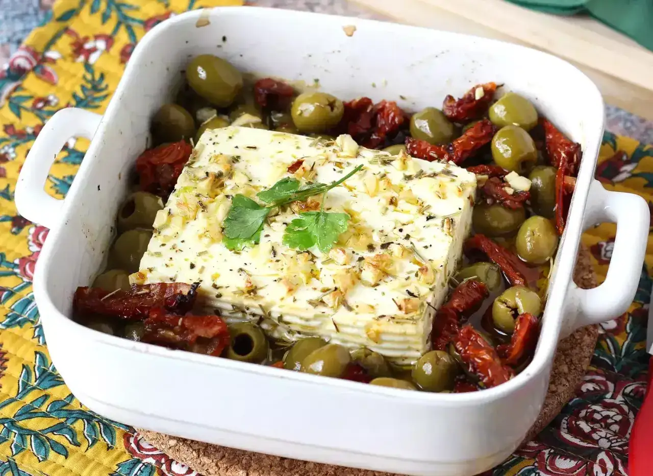 Pieczona feta w oliwie z oliwek, z suszonymi pomidorami i zielonymi oliwkami, posypana ziołami i czosnkiem.