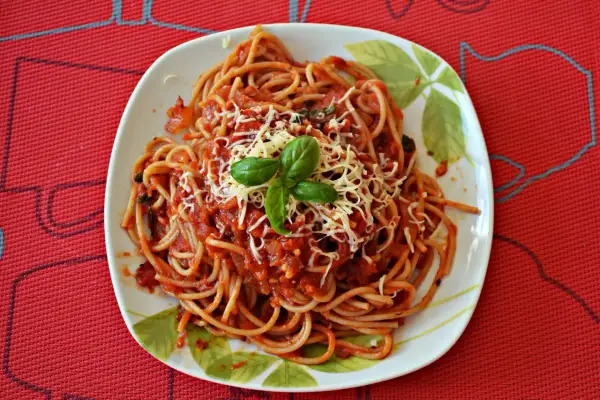 Pyszne spaghetti napoli z sosem pomidorowym, startym serem i listkami bazylii na talerzu.