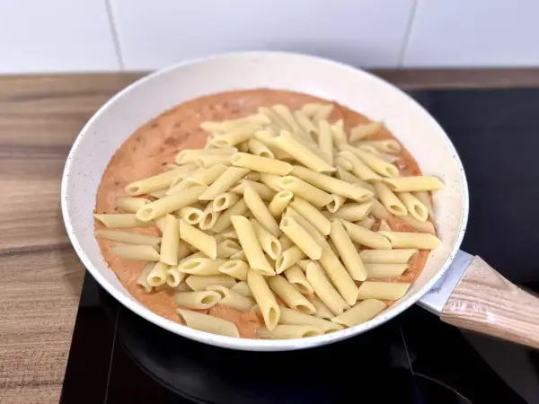 Penne w kremowym sosie pomidorowym z kawałkami chorizo, gotowe do podania.