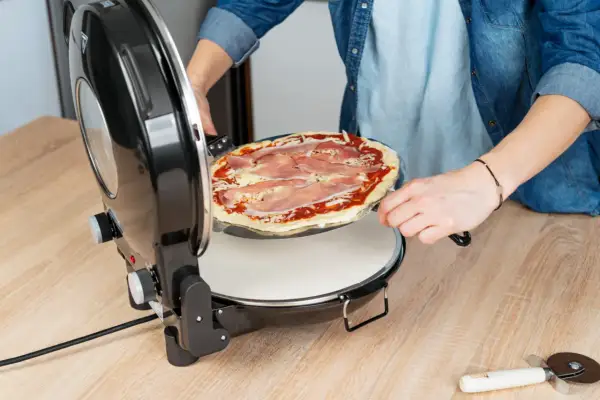 Osoba wkłada pizzę do pieca. Dowiedz się, w jakiej temperaturze piec pizzę, aby uzyskać idealny smak.