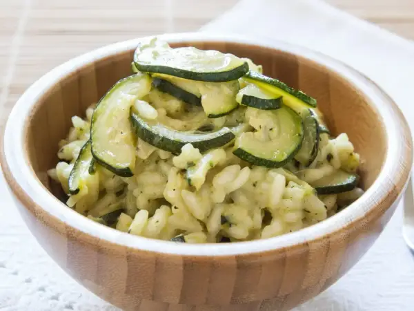 Kremowe risotto z cukinią, podane w drewnianej misce, ozdobione plasterkami zielonej cukinii.