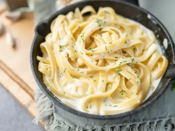 Pyszny makaron fettuccine w kremowym sosie, posypany natką pietruszki. Idealny pomysł, z czym zrobić makaron na szybko.