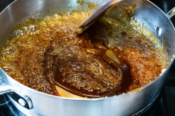 Brązowy, bulgoczący płyn w garnku, to palone masło, które nabiera głębokiego aromatu. Drewniana łyżka miesza je, tworząc karmelowe refleksy.