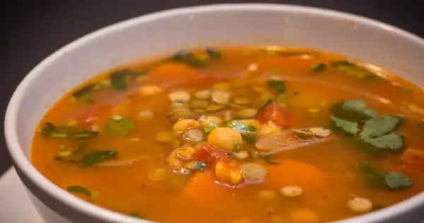 Aromaticzna zupa z ciecierzycy z kawałkami pomidorów, marchewki i świeżą kolendrą.