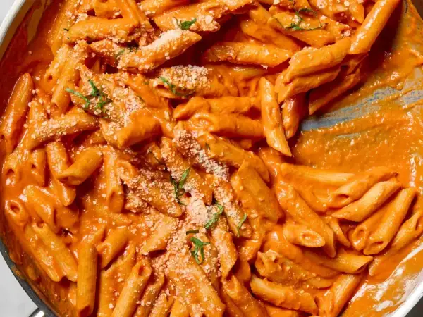 Penne alla vodka w kremowym, pomarańczowym sosie, posypane parmezanem i bazylią. Pyszne danie gotowe do podania.