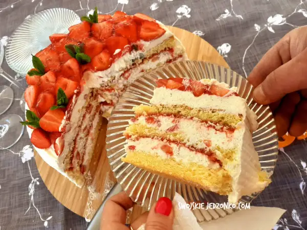 Pyszny tort truskawkowy z bitą śmietaną i świeżymi owocami, kroimy pierwszy kawałek.