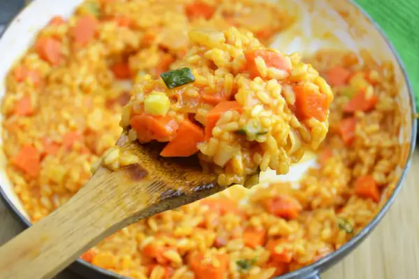 Kremowe risotto pomidorowe z kawałkami marchewki i cukinii, nabierane drewnianą łyżką.