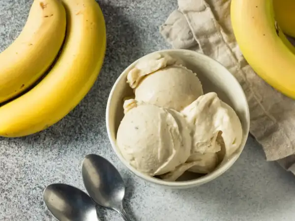 Pyszne lody bananowe w miseczce, obok świeże banany i łyżeczki. Idealne na upalne dni.