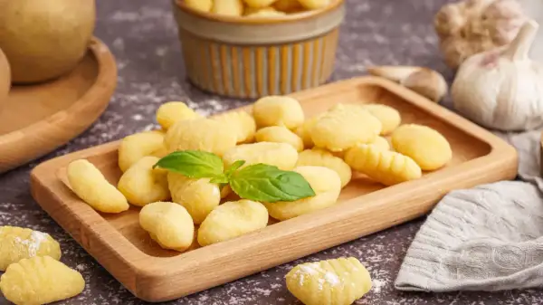 Pyszne, domowe gnocchi na drewnianej desce. Idealny przepis na obiad. W tle czosnek i ziemniaki.
