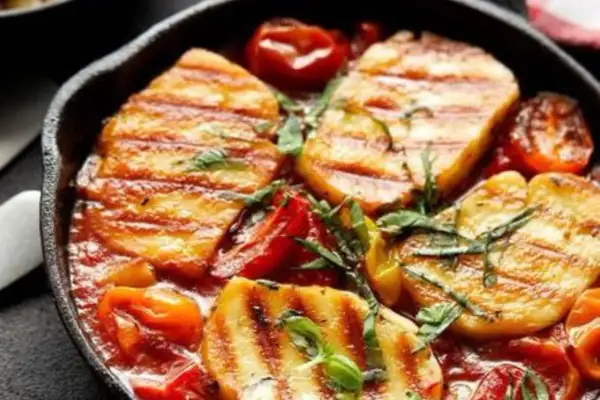 Pyszne halloumi z piekarnika w sosie pomidorowym z ziołami, podane w żeliwnej patelni.