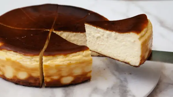 Kawałek pysznego, lekko przypieczonego basque cheesecake jest wyjmowany z całego ciasta.