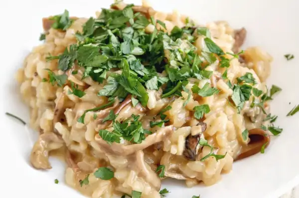 Kremowe risotto z grzybami, posypane świeżą natką pietruszki, wygląda apetycznie.