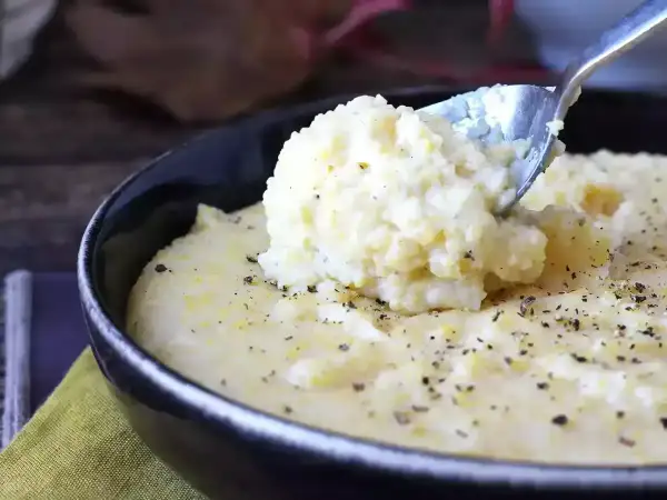 Kremowa polenta, idealna do prostego przepisu. Łyżka wydobywa porcję tej pysznej potrawy, posypanej pieprzem.