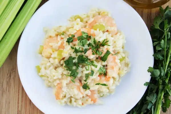 Kremowe risotto z krewetkami, posypane świeżą natką pietruszki, obok łodygi selera i oliwy.
