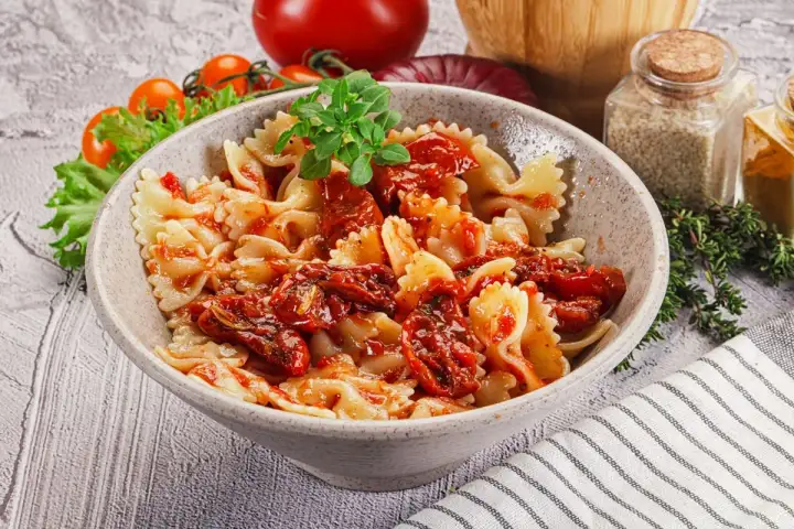 Pyszny makaron farfalle z aromatycznymi suszonymi pomidorami, udekorowany świeżą bazylią.